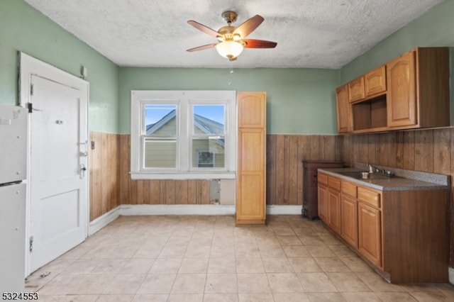 kitchen with a textured ceiling, ceiling fan, wooden walls, and sink