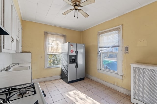 kitchen with radiator heating unit, ceiling fan, stainless steel fridge, light tile patterned floors, and white cabinetry