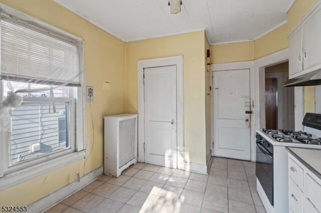 kitchen with white cabinetry, gas range gas stove, light tile patterned flooring, and ornamental molding