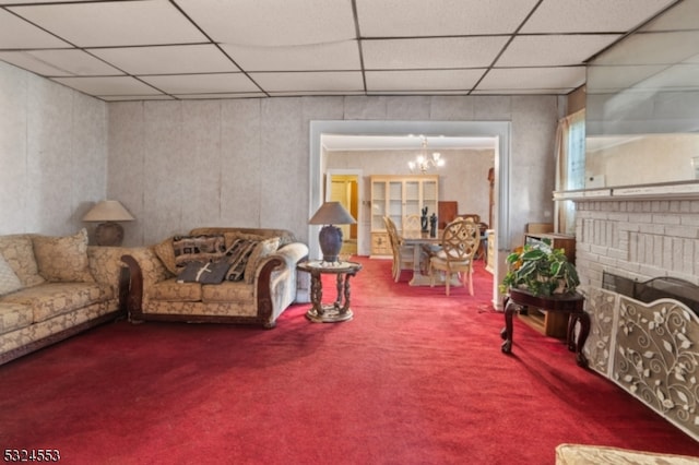 living room featuring a paneled ceiling, carpet floors, a fireplace, and an inviting chandelier