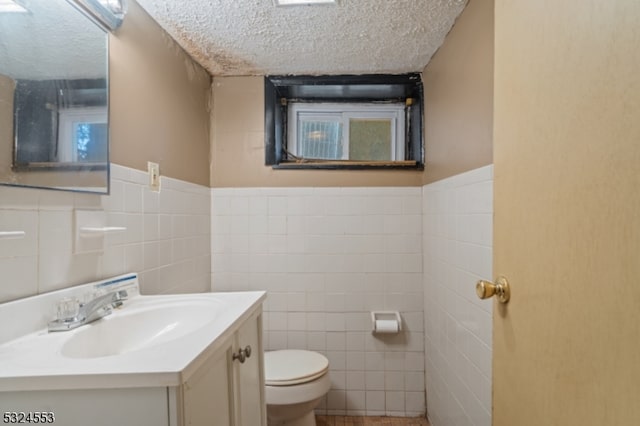 bathroom with a textured ceiling, vanity, toilet, and tile walls