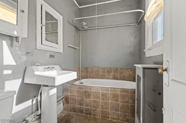 bathroom featuring tiled shower / bath combo, toilet, and a wealth of natural light