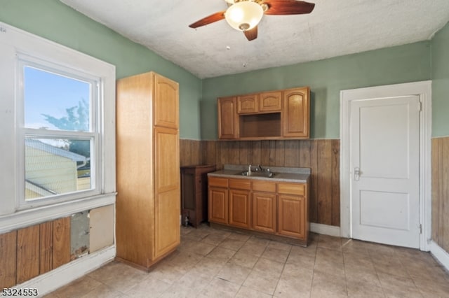 kitchen featuring a textured ceiling, ceiling fan, wood walls, and sink