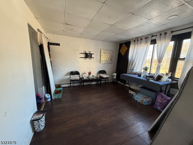 sitting room with a paneled ceiling, dark hardwood / wood-style floors, and brick wall