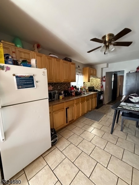 kitchen with backsplash, black range oven, ceiling fan, sink, and white fridge