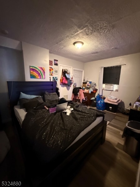 bedroom with hardwood / wood-style flooring, cooling unit, and a textured ceiling