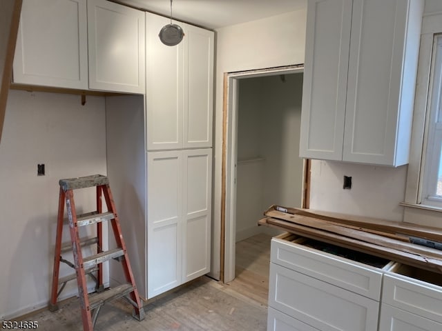 kitchen with light wood-type flooring, white cabinetry, and hanging light fixtures