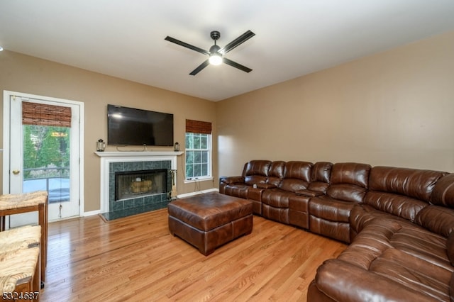 living room featuring ceiling fan, light hardwood / wood-style floors, and a tiled fireplace