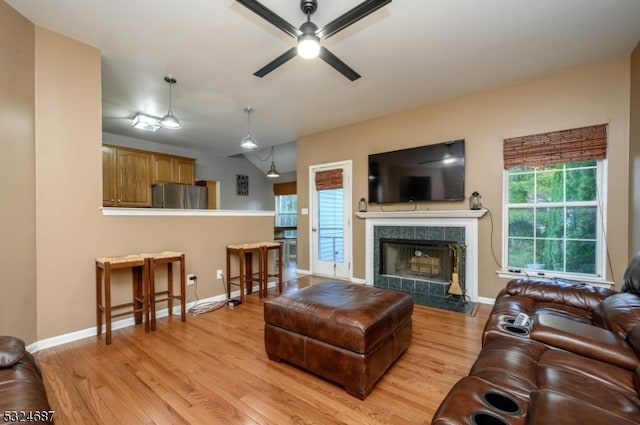 living room featuring ceiling fan, a tile fireplace, a wealth of natural light, and light hardwood / wood-style flooring