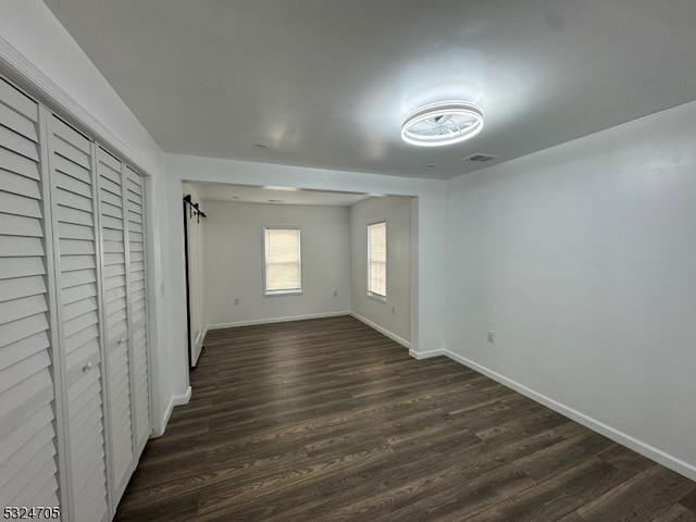 unfurnished bedroom with a barn door, dark wood-type flooring, and a closet