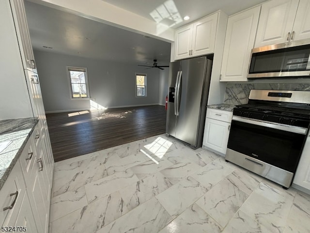 kitchen with appliances with stainless steel finishes, light stone counters, ceiling fan, white cabinets, and light hardwood / wood-style floors