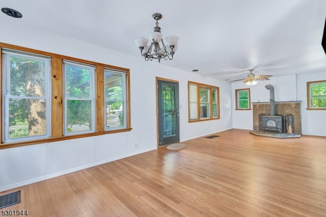 unfurnished living room with ceiling fan with notable chandelier, light wood-type flooring, and a wood stove