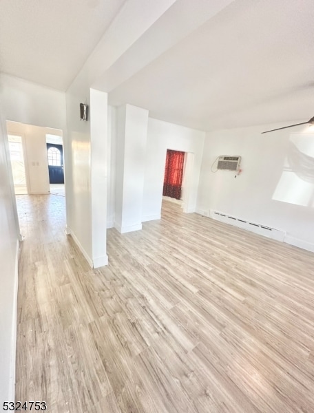 empty room featuring a wall mounted air conditioner, ceiling fan, a baseboard radiator, and light hardwood / wood-style flooring