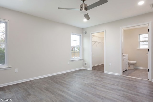 unfurnished bedroom featuring ensuite bathroom, ceiling fan, a walk in closet, and multiple windows