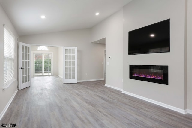 unfurnished living room featuring vaulted ceiling, light hardwood / wood-style flooring, and french doors