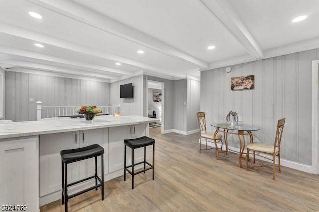 kitchen featuring wooden walls, a breakfast bar, beamed ceiling, and light hardwood / wood-style floors