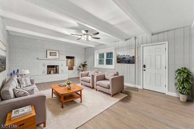 living room with beam ceiling, a brick fireplace, ceiling fan, and light wood-type flooring