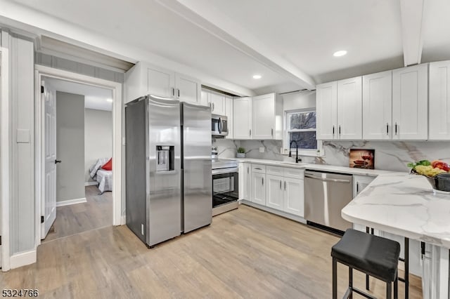 kitchen featuring white cabinets, sink, light wood-type flooring, appliances with stainless steel finishes, and beam ceiling