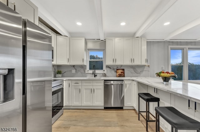 kitchen featuring appliances with stainless steel finishes, light wood-type flooring, white cabinets, sink, and beamed ceiling