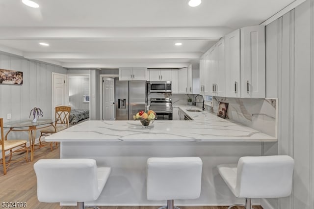 kitchen featuring a kitchen bar, kitchen peninsula, white cabinetry, and stainless steel appliances