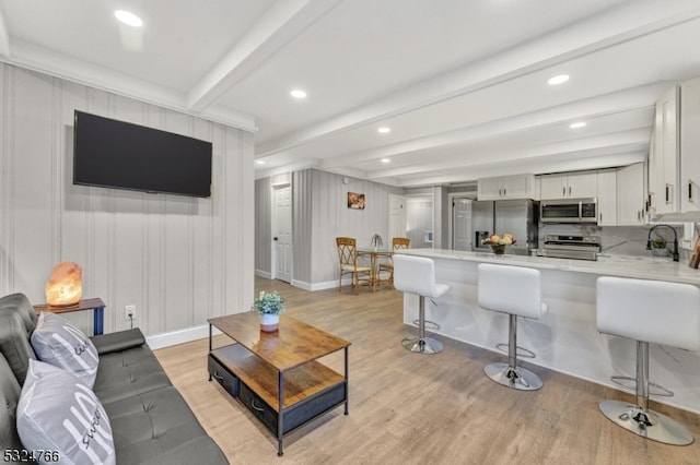 living room featuring beamed ceiling, light hardwood / wood-style floors, and sink