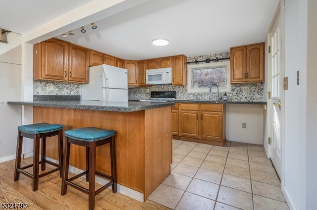 kitchen with kitchen peninsula, a kitchen bar, white appliances, and tasteful backsplash