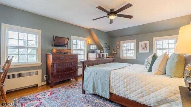 bedroom with a ceiling fan, radiator, vaulted ceiling, and light wood-style flooring