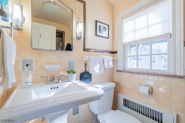 half bath featuring radiator heating unit, a sink, toilet, and tile walls