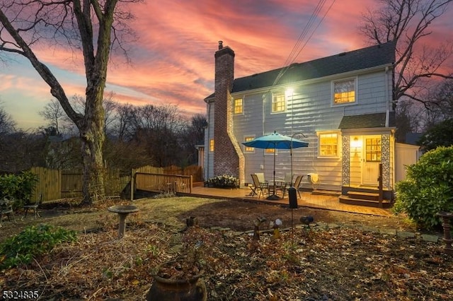 back of house at dusk featuring entry steps, a chimney, a patio area, and fence