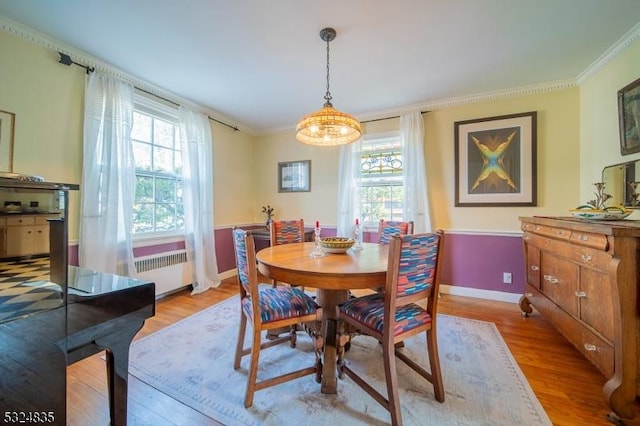 dining space with light wood-style floors, radiator, ornamental molding, and baseboards