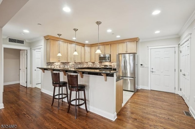 kitchen with dark countertops, appliances with stainless steel finishes, a breakfast bar, dark wood-style flooring, and a peninsula