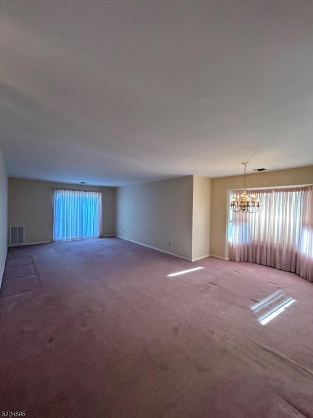 carpeted empty room featuring an inviting chandelier