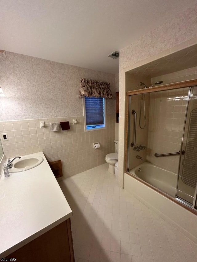 full bathroom with tile patterned floors, bath / shower combo with glass door, vanity, tile walls, and toilet