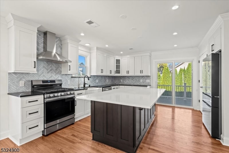 kitchen featuring wall chimney range hood, a kitchen island, light hardwood / wood-style flooring, white cabinets, and appliances with stainless steel finishes