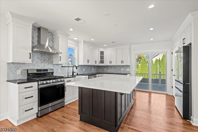 kitchen featuring wall chimney range hood, a kitchen island, light hardwood / wood-style flooring, white cabinets, and appliances with stainless steel finishes