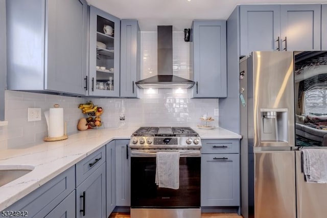 kitchen with gray cabinets, stainless steel appliances, light stone counters, decorative backsplash, and wall chimney exhaust hood