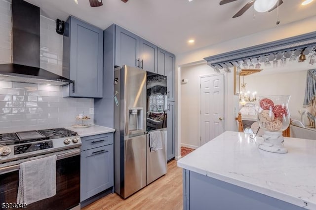 kitchen featuring tasteful backsplash, ceiling fan, stainless steel appliances, light wood-type flooring, and wall chimney exhaust hood