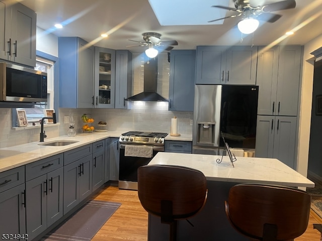 kitchen with decorative backsplash, stainless steel appliances, wall chimney range hood, sink, and light hardwood / wood-style flooring