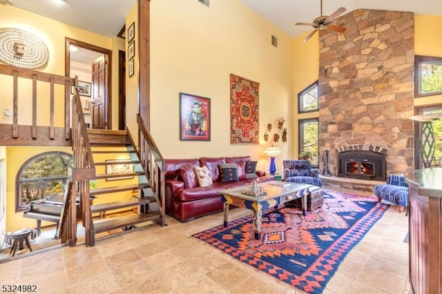 living room with a stone fireplace, ceiling fan, and high vaulted ceiling