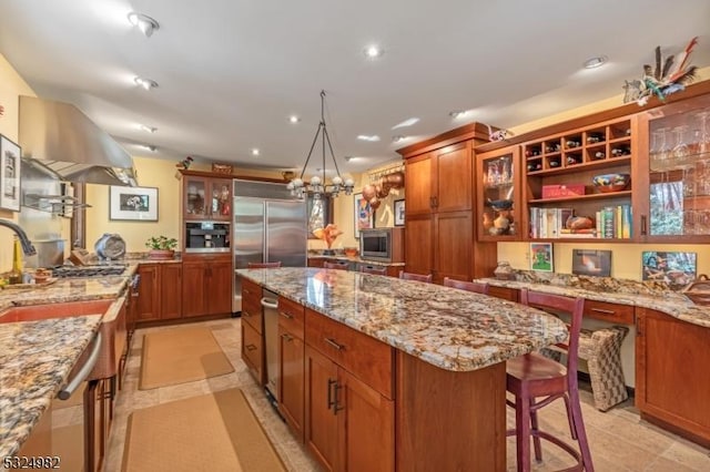 kitchen with a center island, a kitchen breakfast bar, built in appliances, a chandelier, and extractor fan