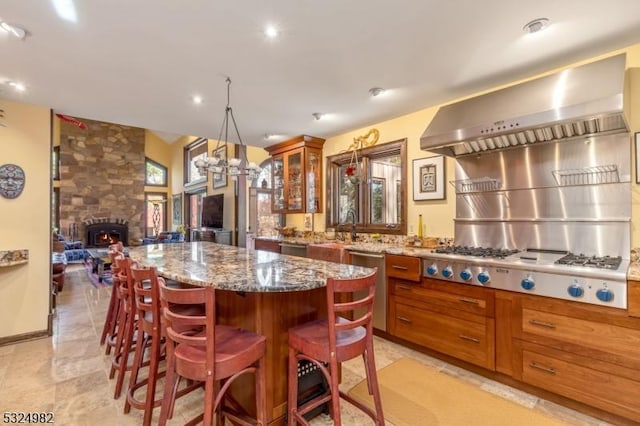 kitchen with a center island, exhaust hood, a fireplace, light stone counters, and stainless steel appliances