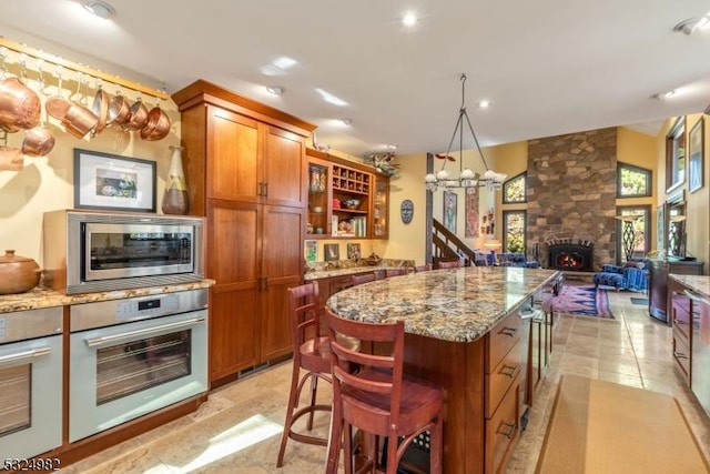 kitchen featuring a stone fireplace, a breakfast bar area, light stone countertops, a kitchen island, and stainless steel appliances