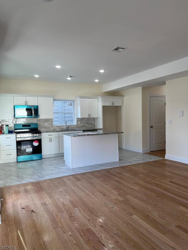 kitchen with a center island, backsplash, light hardwood / wood-style floors, white cabinets, and appliances with stainless steel finishes