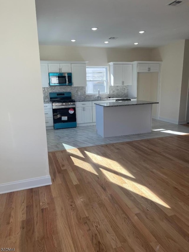 kitchen with white cabinetry, stainless steel appliances, tasteful backsplash, light hardwood / wood-style flooring, and a kitchen island