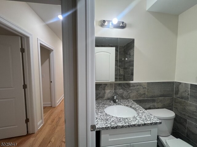 bathroom featuring hardwood / wood-style flooring, vanity, toilet, and tile walls