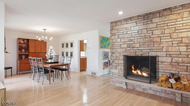 dining room featuring a stone fireplace, light hardwood / wood-style flooring, and an inviting chandelier