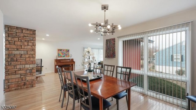 dining area with light hardwood / wood-style floors, a wood stove, a wealth of natural light, and an inviting chandelier