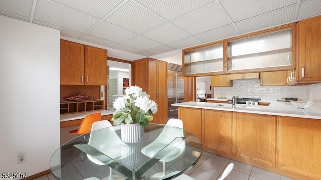 kitchen featuring a drop ceiling, built in refrigerator, light tile patterned floors, tasteful backsplash, and kitchen peninsula