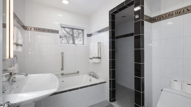 bathroom with tiled tub, toilet, tile walls, and sink