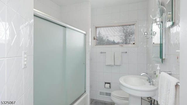 full bathroom with a wealth of natural light, toilet, tile walls, and combined bath / shower with glass door